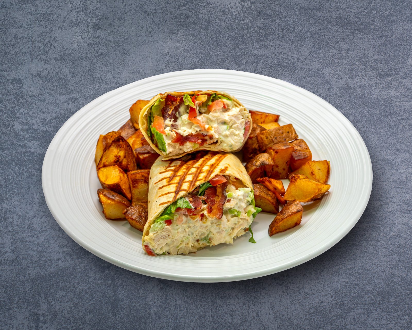 Grilled chicken salad wrap with bacon, lettuce, tomato, and a side of roasted potatoes, served at a restaurant in downtown Chattanooga.