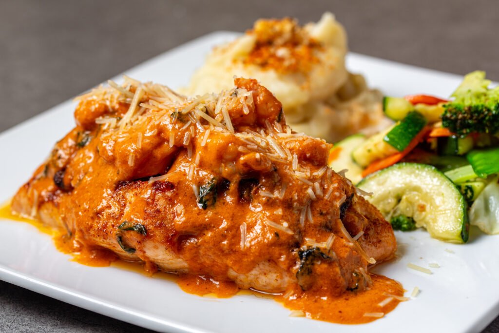 Delicious Salmon Monte Carlo topped with a creamy, cheesy sauce, served with mashed potatoes and fresh vegetables at a fine dining restaurant in Lee Highway Chattanooga.