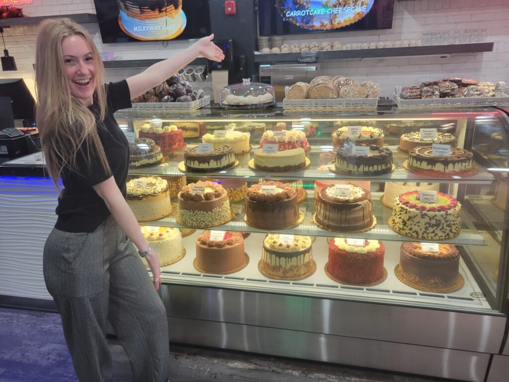 Smiling staff member at City Cafe in Chattanooga showcasing a colorful cake display inside one of the most popular breakfast and brunch restaurants downtown Chattanooga.